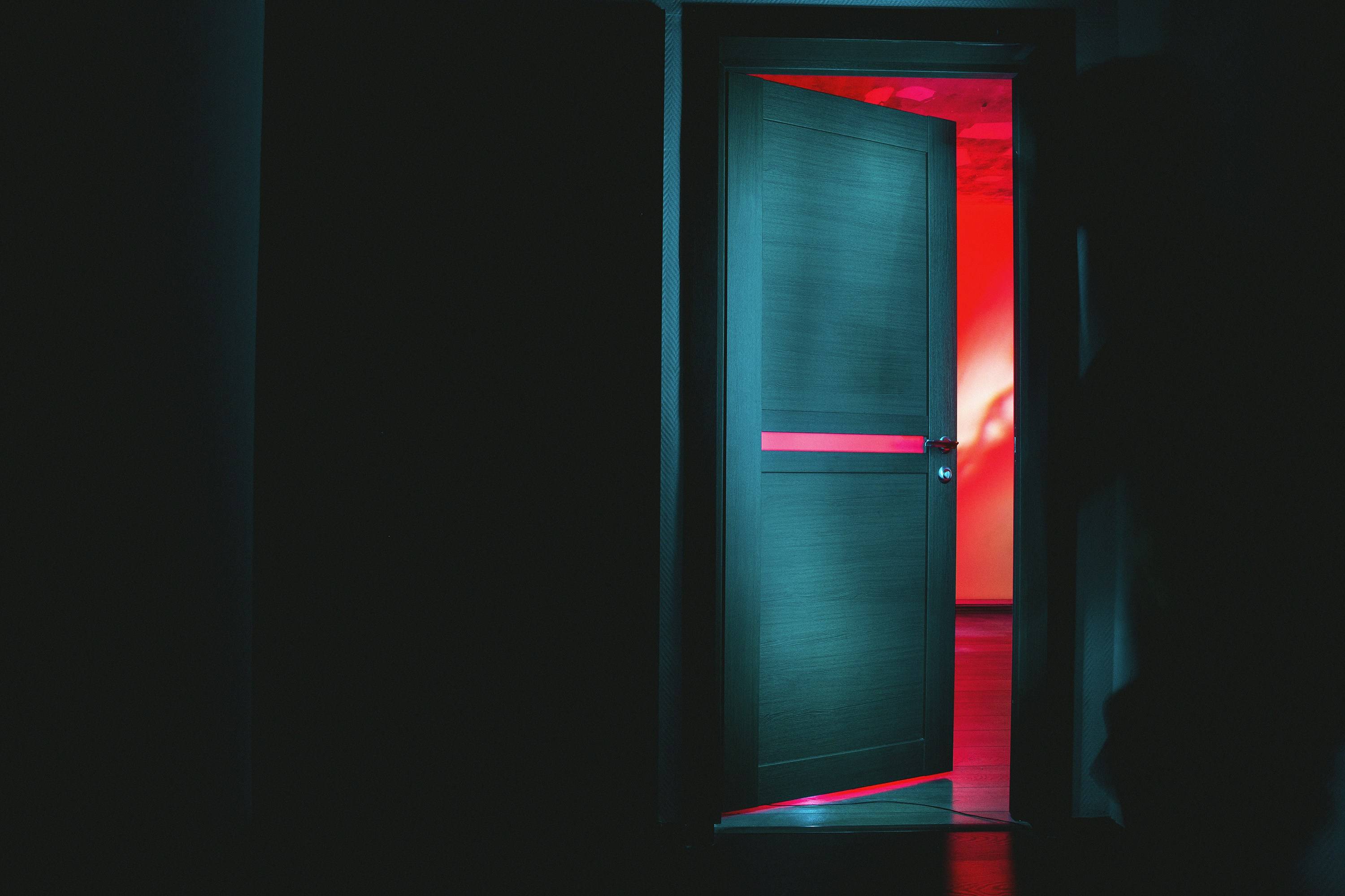 Dark hallway with partially open door revealing red light, suggesting sound leaking through an unsealed door