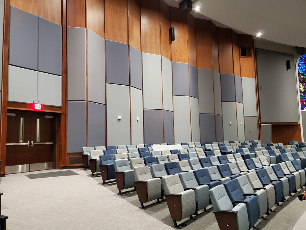 Church auditorium with grey acoustic panels installed on wood-paneled walls and blue-grey upholstered seating