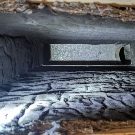 Inside view of dusty HVAC duct showing heavy grey dust and debris buildup on interior walls