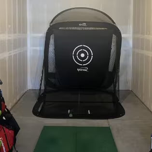 Indoor golf simulator setup with hitting mat and practice net in a garage, showing a home golf simulation space