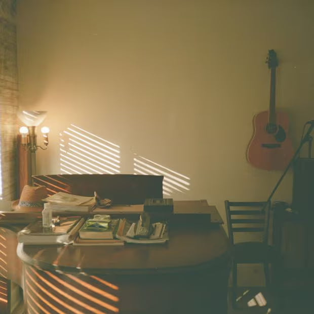 Sunlit music room with acoustic guitar on wall, books and papers on round table, warm afternoon light