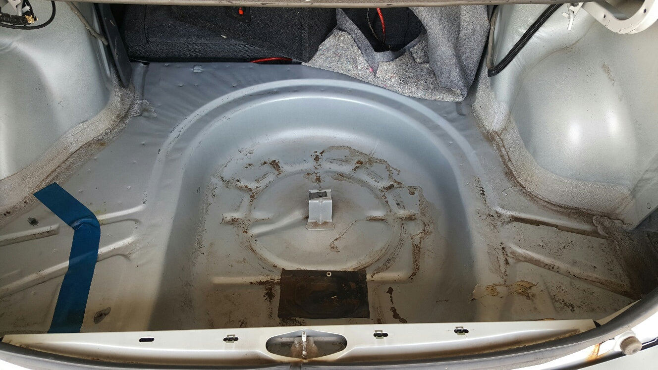 Bare metal trunk floor of Chevy Cavalier with rust residue, before soundproofing installation