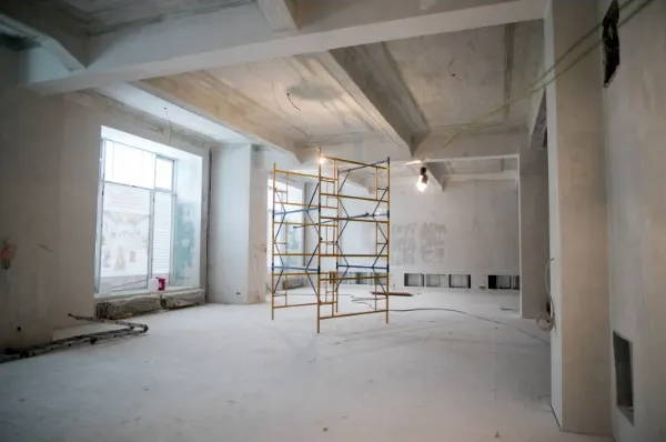 Interior construction space with scaffolding, bare walls, and exposed ceiling beams during renovation