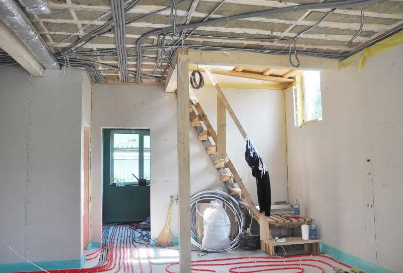 Home under construction showing radiant floor heating tubing and exposed ceiling wiring, ready for soundproofing