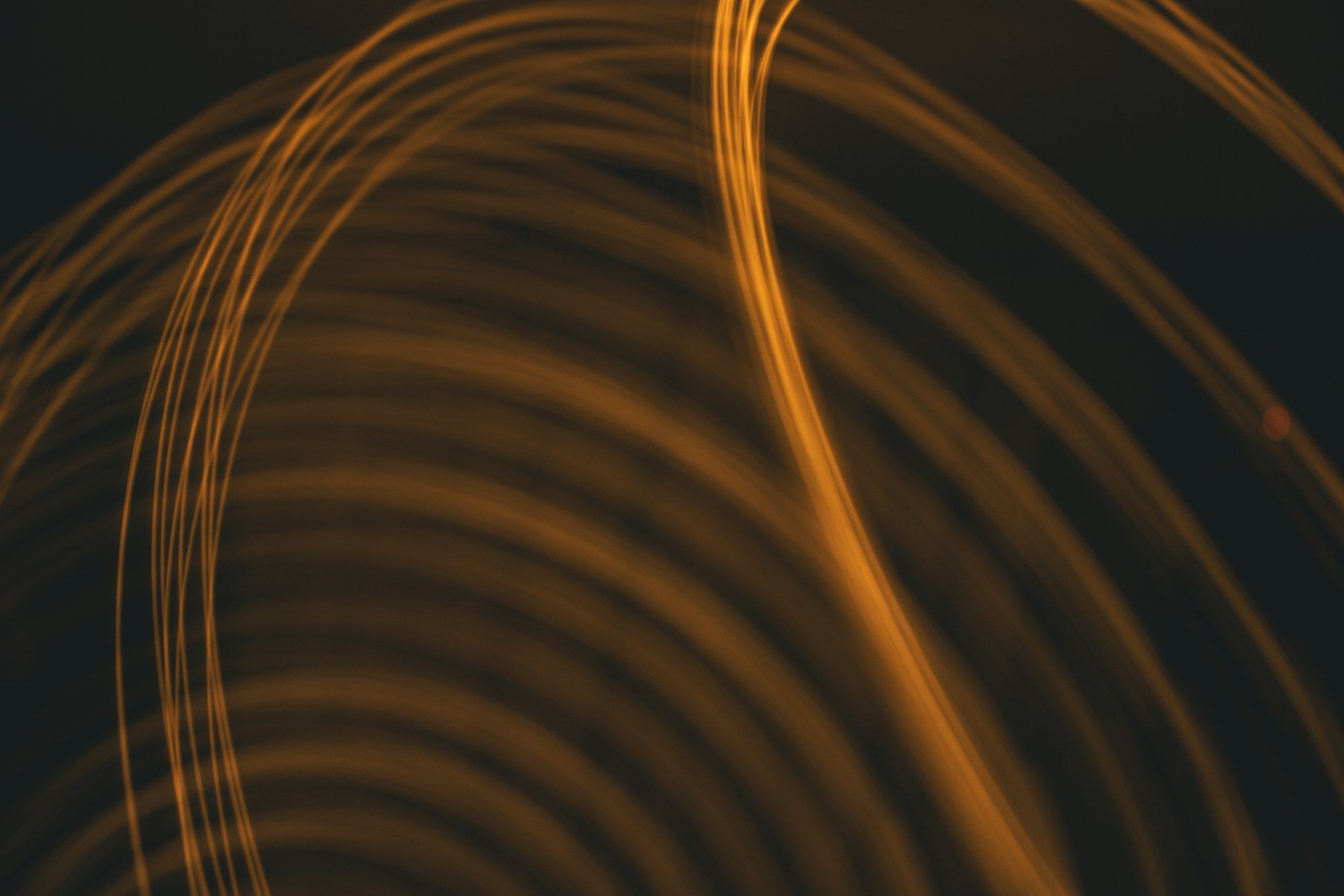 Abstract golden light trails forming circular waves against dark background