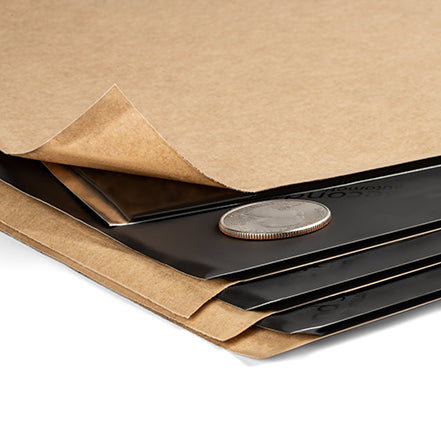 Damplifier Pro sound deadening sheets with kraft paper liner, black foil face, stacked with coin for scale