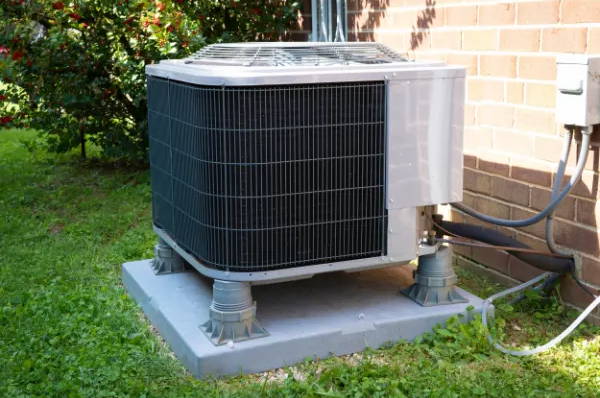 Outdoor residential AC condenser unit beside brick wall, illustrating noise source for soundproofing solutions