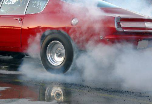 Red muscle car doing a burnout on a drag strip, generating tire smoke