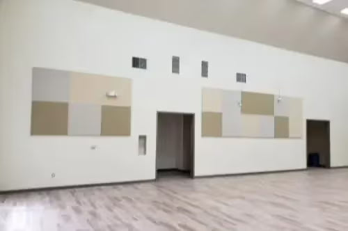 Large room with white walls and wooden flooring, featuring acoustic panels.