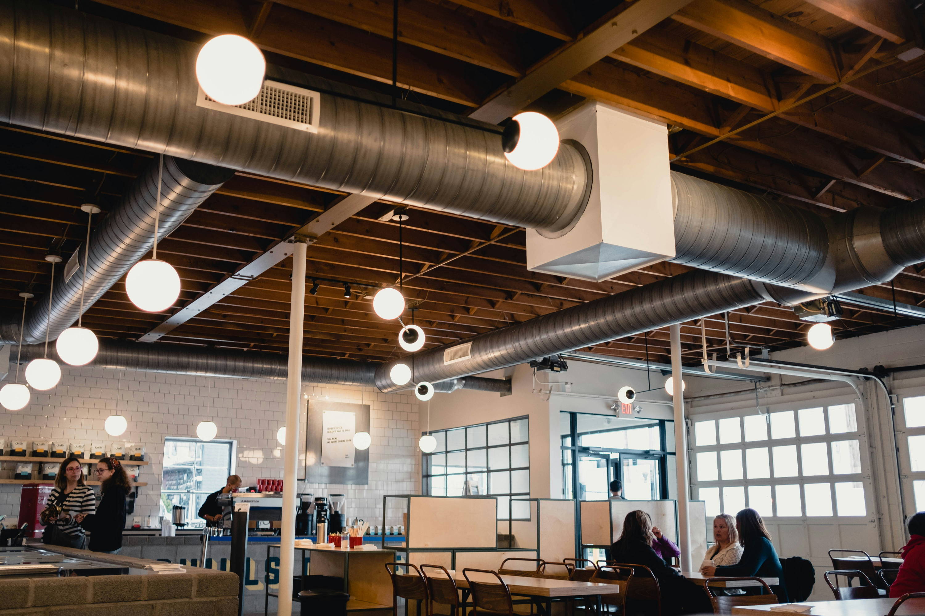 Industrial café ceiling with exposed HVAC ductwork, wood beams, and globe pendant lights — untreated space