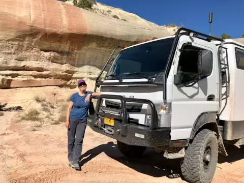 Woman standing beside a white 4x4 overland truck in a desert canyon, showcasing vehicle soundproofing kit use case