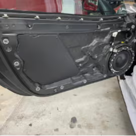 Car door inner panel with speaker installed, showing soundproofing treatment with black deadening mat applied