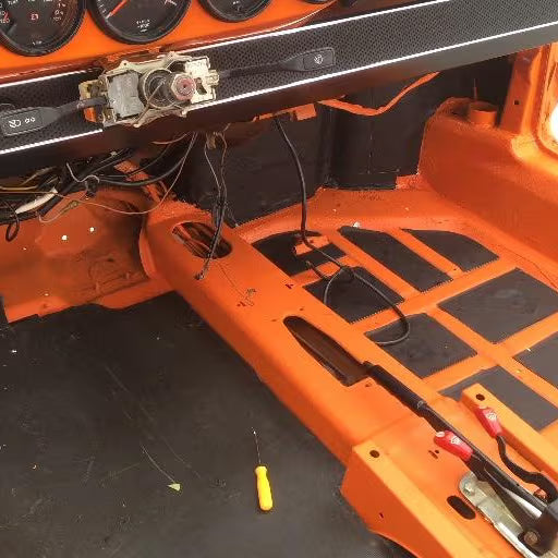 Stripped orange car interior floor with sound deadening mat partially installed on floorpan
