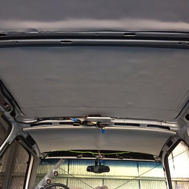 Vehicle headliner installed over roof with wiring visible on crossbar, interior soundproofing application