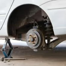 Car wheel well with brake rotor exposed, tire removed, vehicle on jack stand for soundproofing installation