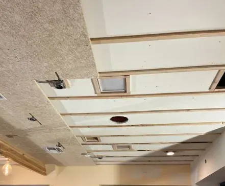 Wood slat ceiling panels partially installed with acoustic treatment visible above, showing in-progress ceiling soundproofing project